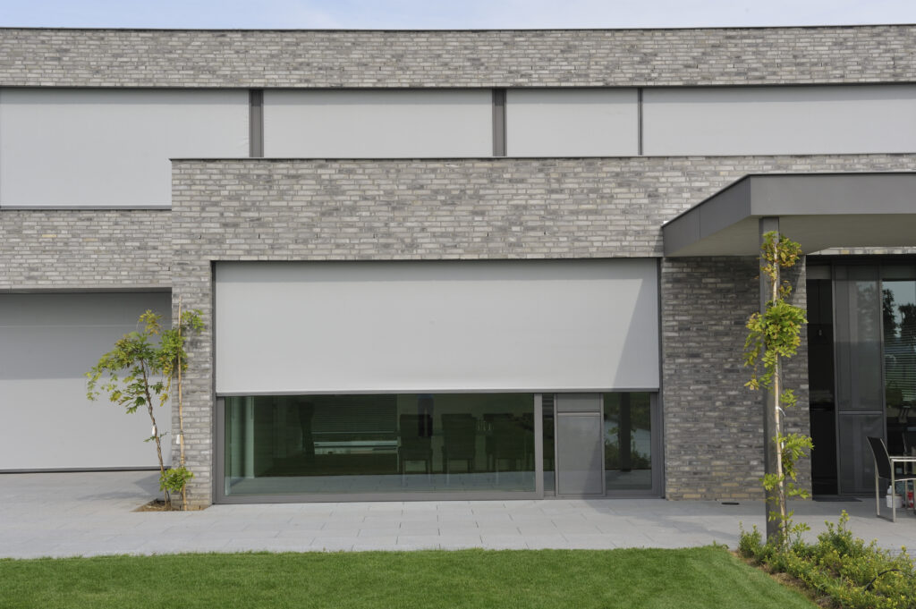 Modern building with a grey external fabric screens partially covering a large ground-floor window.