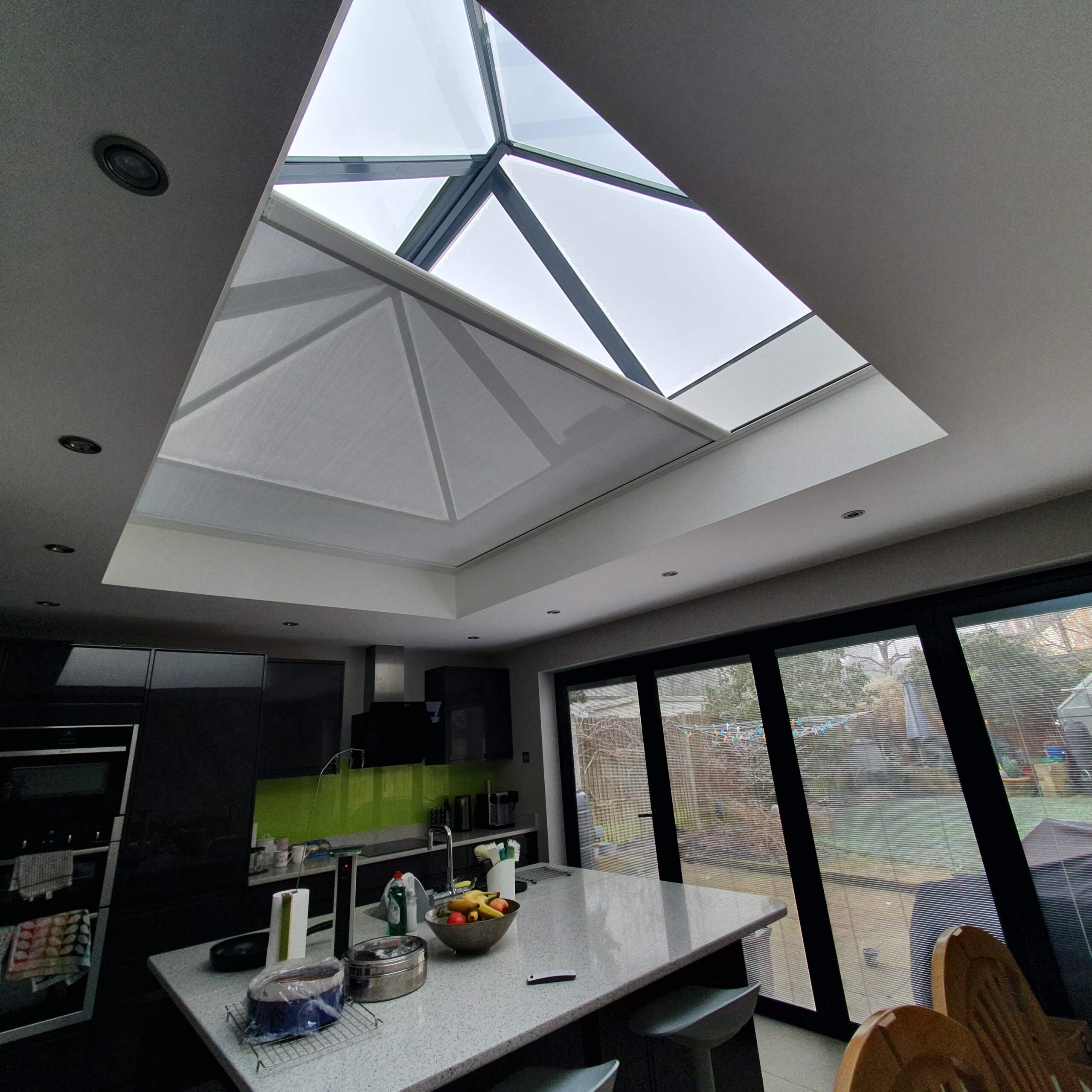 A modern kitchen with a large roof light and full‑height glazing, showing a bright and comfortable space supported by a high‑performance shading solution.