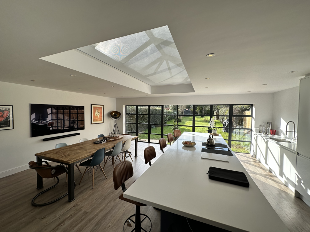 A bright open‑plan kitchen and dining space with large glazing and roof lights, showing a comfortable, well‑lit room enhanced by a high‑end shading solution.