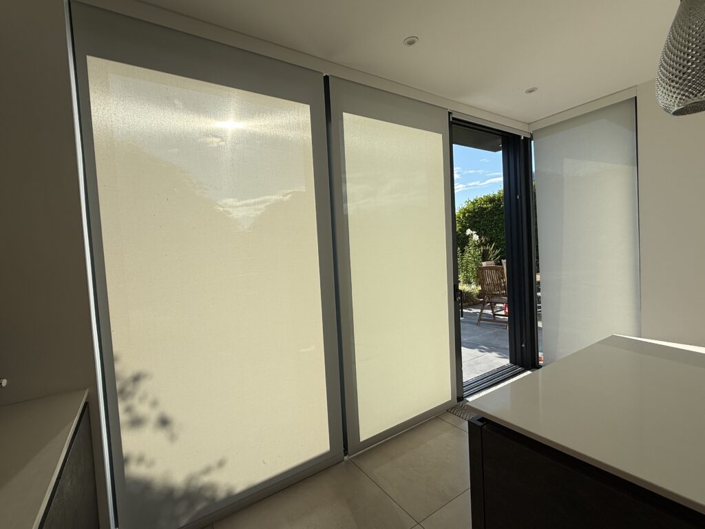 Floor-to-ceiling bifold and sliding glass doors fitted with translucent electric blinds in Caroline and Mike’s Bournemouth home. Sunlight filters through, highlighting the seamless indoor-outdoor connection and year-round comfort.