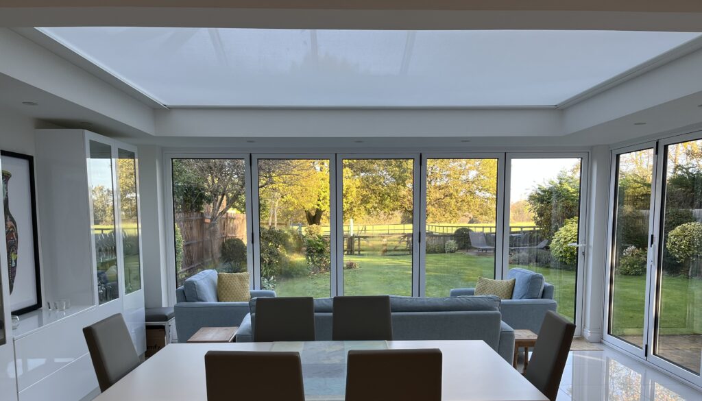 Modern dining and living space with large skylight and garden views, featuring concealed roof blind integration.