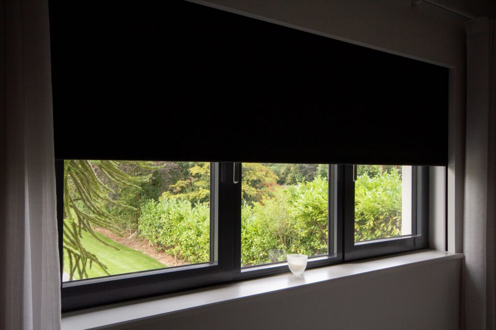 A sleek black blackout blind partially drawn inside a modern room, seamlessly concealed within the window frame, with lush greenery visible outside.