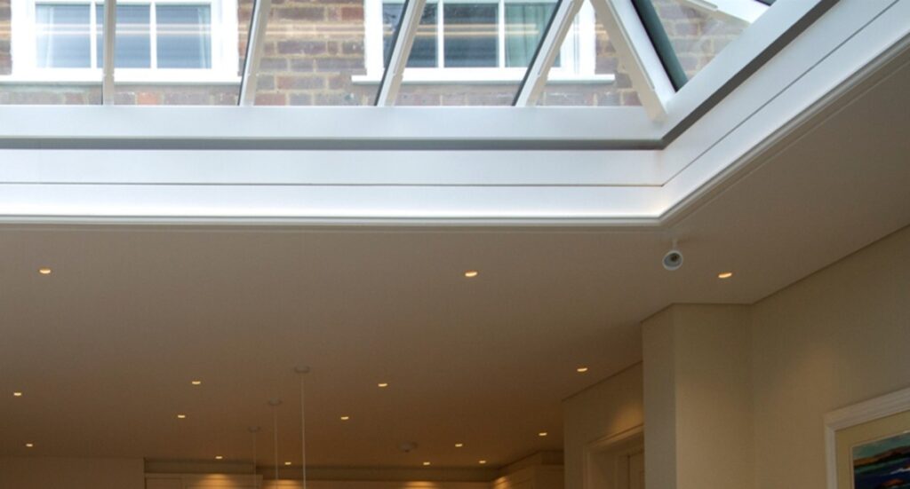 A spacious living area with a large roof lantern above, seamlessly integrated into the ceiling. The XL Hercules roof blind is fully concealed within C190 × 340 Blindspace boxes, with no visible hardware or fixings.