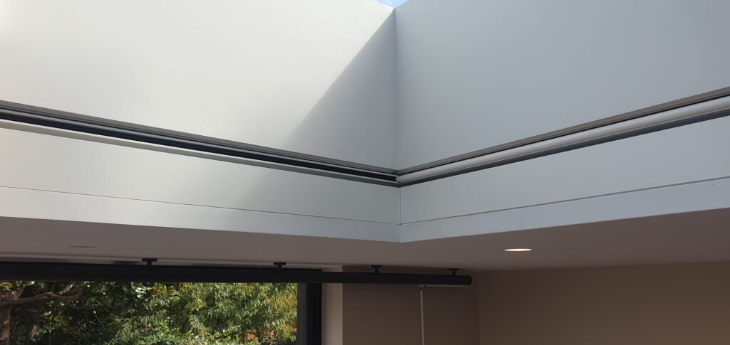 A minimalist London apartment featuring a recessed roof light with concealed blind hardware. The skylight spans 4 m and is integrated into a sharp, angular ceiling design. No visible blind components are present, showcasing a seamless architectural finish.