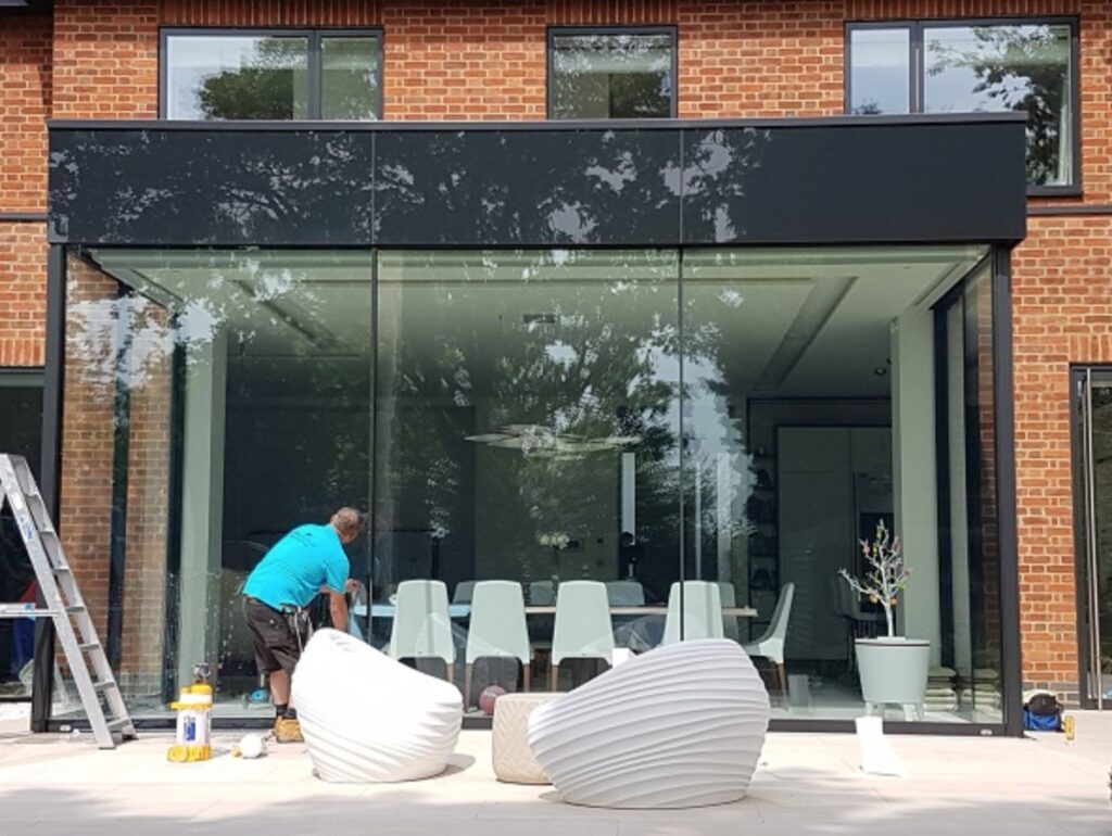 Mike, WindowTreat’s expert installer, applying 3M Prestige 70 Exterior window film to large glass doors of a modern brick home to reduce solar heat gain while maintaining a clear, natural appearance.
