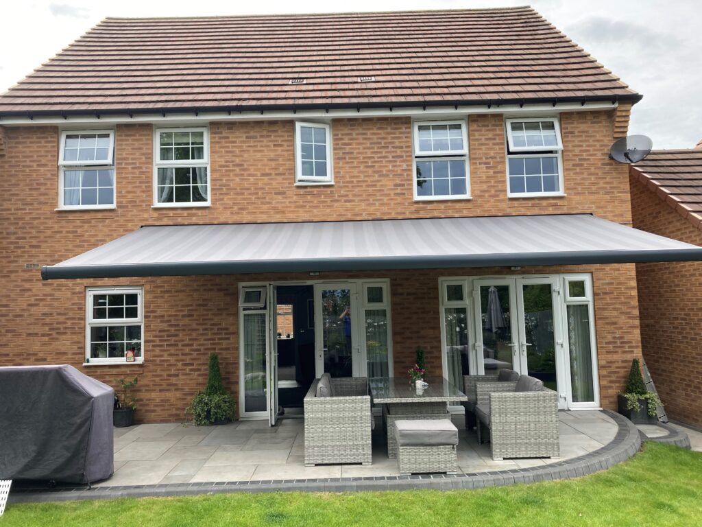 Rear view of a brick house with a large 7m wide, 3.1m projection multi-fix awning shading the patio and helping cool the living area in summer.