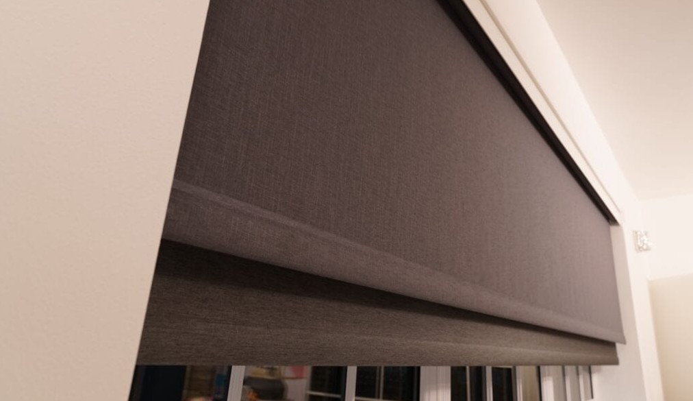 Window fitted with dual freehanging blinds, one sheer and one dim-out, partially lowered to show layered light control. Both blinds operate independently and retract into a concealed pocket above the frame.