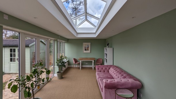 Bright multi use extension with a large roof lantern, pastel green walls and side glazing, shown with all blackout blinds fully retracted to reveal an open, light filled space.